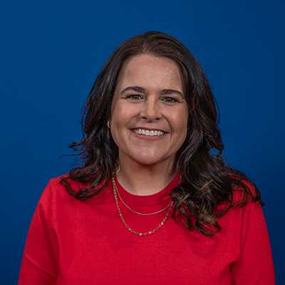 A middle-aged light skinned white and Native American female with brown shoulder length hair and brown eyes, wearing a red sweater.