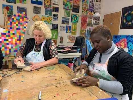 A white and an African woman sit at a table doing crafts